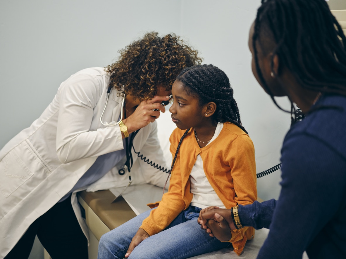 Young girl holding her mom's hand during an ear exam.