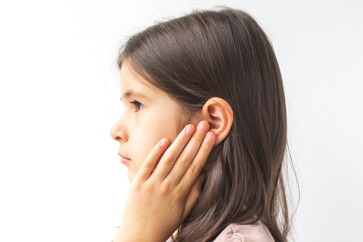 Young girl with her hand on her ear looking upset