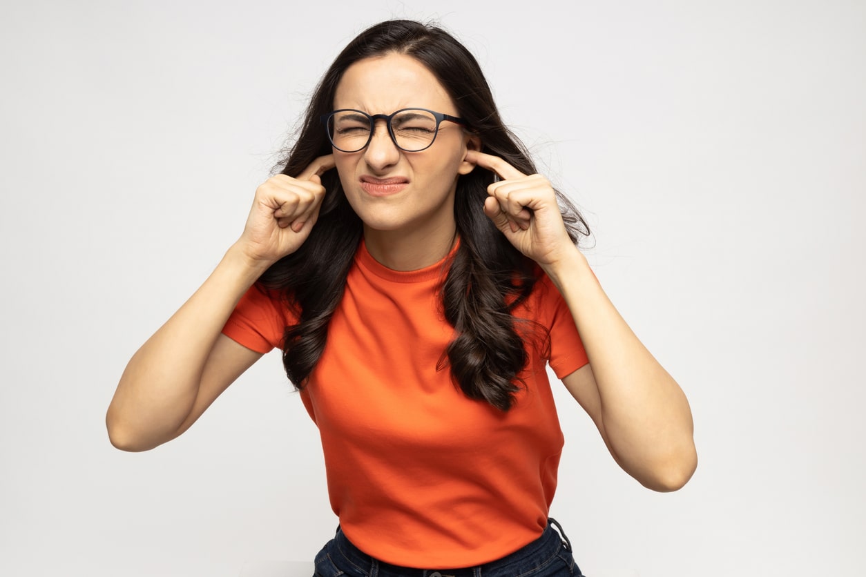 Young woman on a white background plugging her ears.