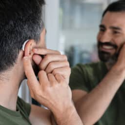 Man with BTE hearing aid looks at herself in mirror and tries on hearing device.