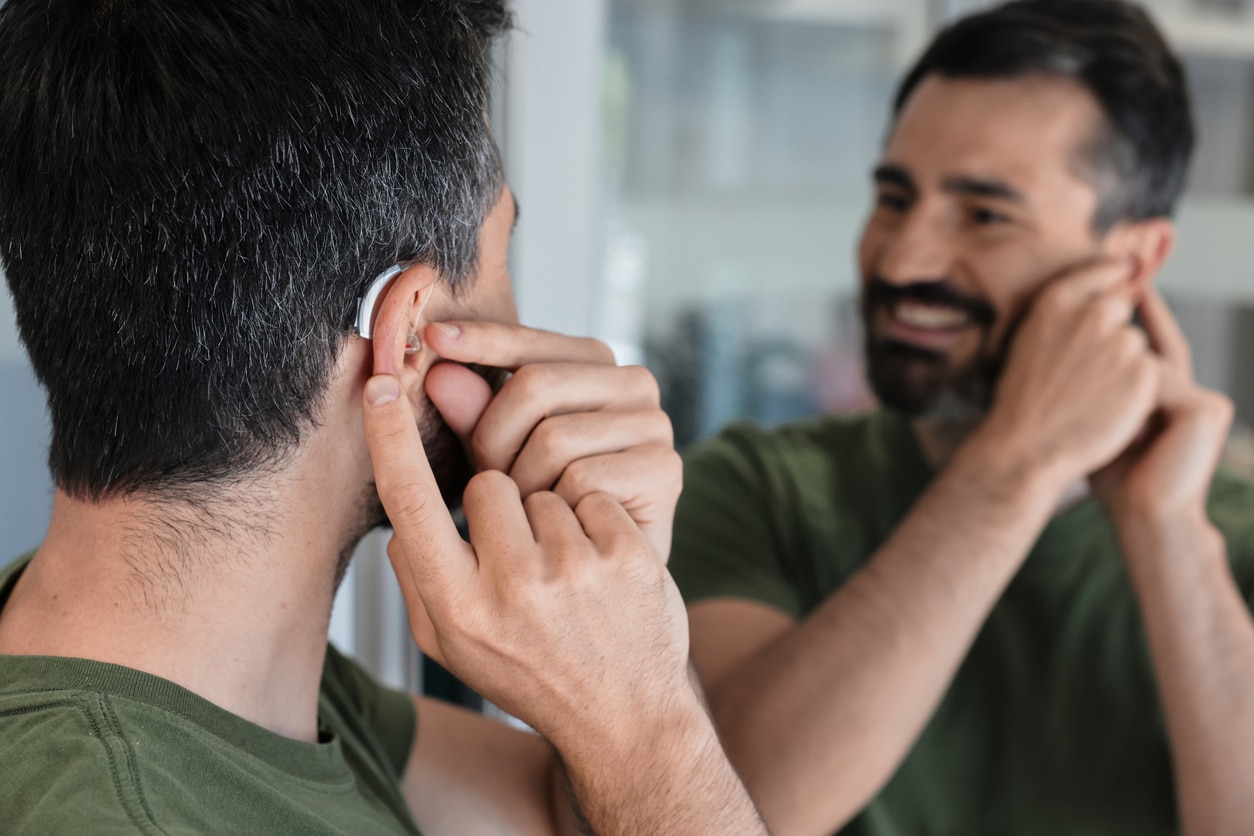 Man with BTE hearing aid looks at herself in mirror and tries on hearing device.