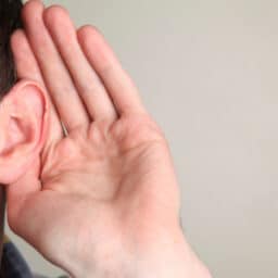 Man holding a hand up to his ear, listening.