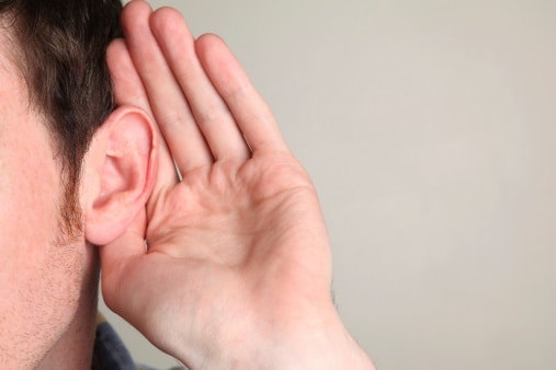 Man holding a hand up to his ear, listening.
