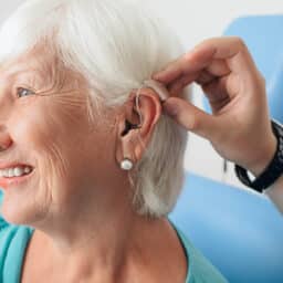 Doctor helping a senior patient put on their hearing aid.