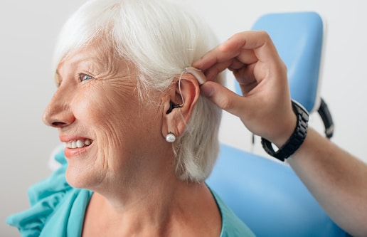 Doctor helping a senior patient put on their hearing aid.