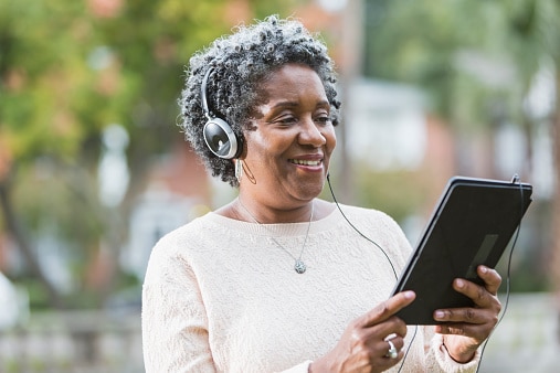Senior woman listening to her audiobook while following along on her e-reader.